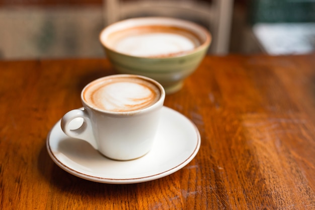 Duas xícaras de cappuccino com latte art na mesa de madeira. Conceito de pequeno-almoço fácil. Copos de cerâmica pequenos e grandes