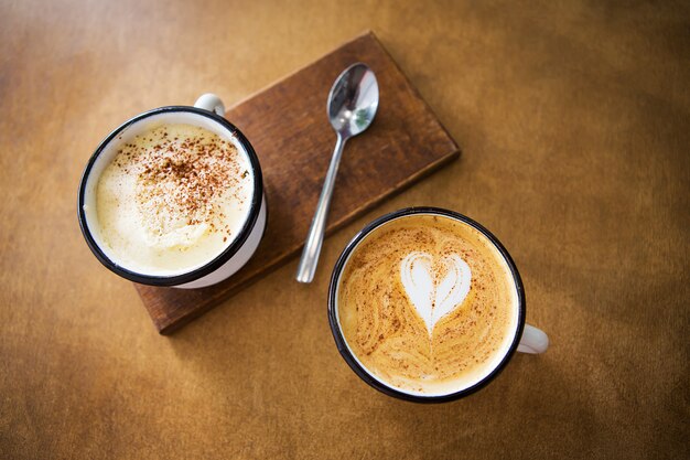 Duas xícaras de cappuccino e café com leite estão sobre uma mesa de madeira
