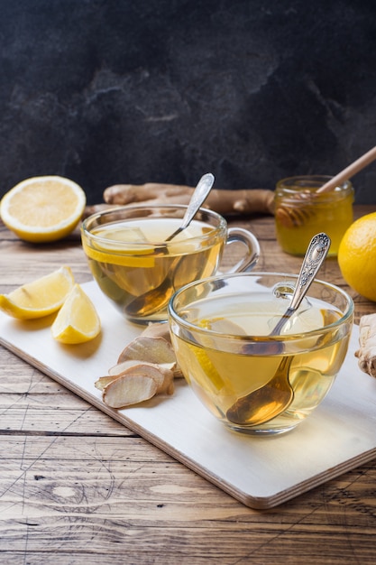 Foto duas xícaras de chá de ervas naturais gengibre limão e mel numa superfície de madeira.