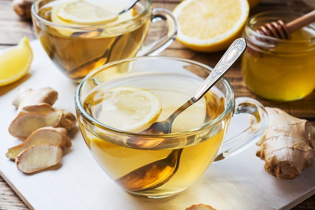 Duas xícaras de chá de gengibre natural limão limão e mel em um fundo de madeira.