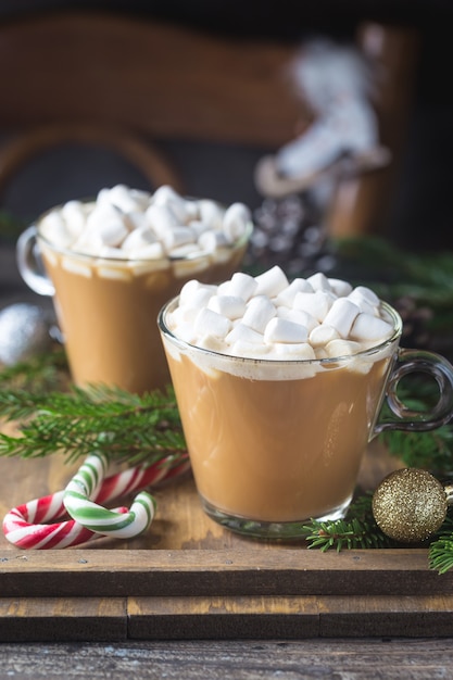 Duas xícaras de chocolate cacau com marshmallow em uma madeira com enfeites de natal