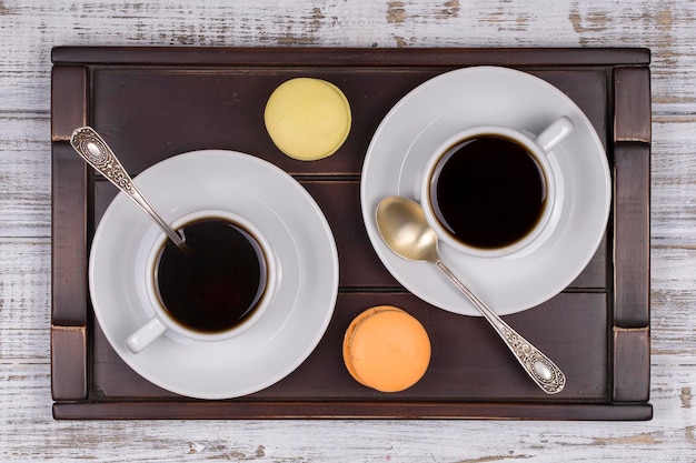 Duas xícaras de colher de café e bolos de macaron na bandeja na mesa de madeira branca Conceito de estilo de vida Close-up Vista superior