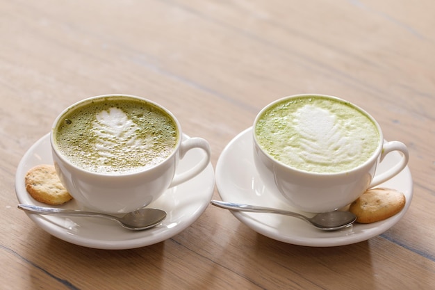 Duas xícaras de matcha latte com latte art na mesa de madeira