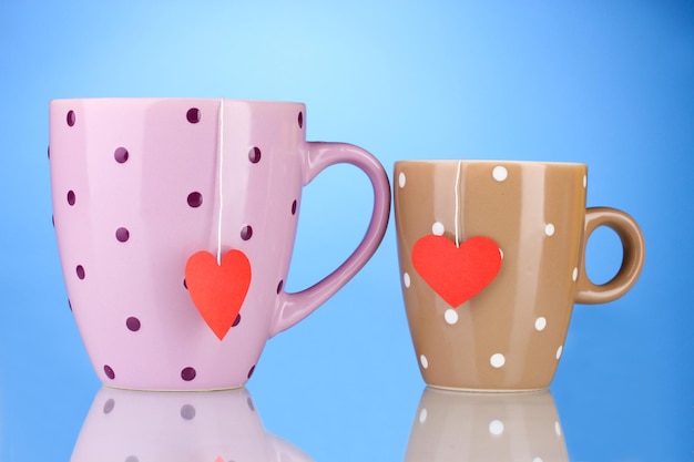 Duas xícaras e saquinhos de chá com etiqueta vermelha em forma de coração sobre fundo azul