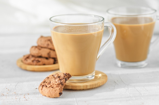 Duas xícaras transparentes de café com leite com biscoitos de chocolate fresco nas sombras da manhã e raios solares em cima da mesa