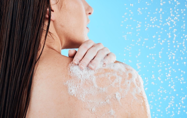 Foto dúchese las manos y el lavado de espalda de una mujer en un estudio con un cuidado corporal femenino para la rutina de belleza modelo de agua y bienestar de una persona joven que limpia con jabón para la higiene y el aseo con fondo azul