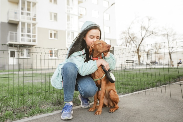 La dueña abraza a un perro con el telón de fondo de un fondo de la ciudad.