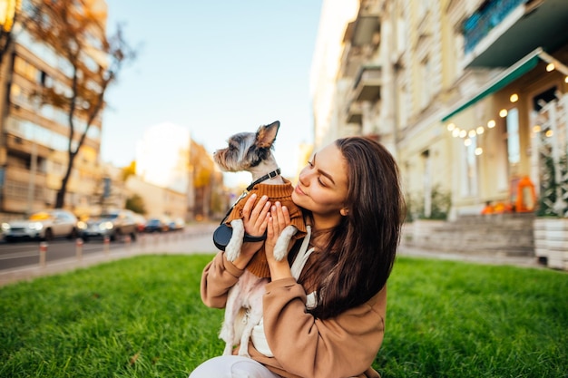 Foto dueña de una perra vestida de forma informal sosteniendo a su lindo yorkshire terrier y sentada en el césped