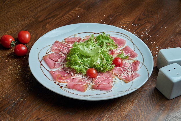Dünn geschnittenes Thunfisch-Carpaccio mit Salat, Kirschtomaten und Parmesan auf einem weißen Teller. Frische Meeresfrüchte