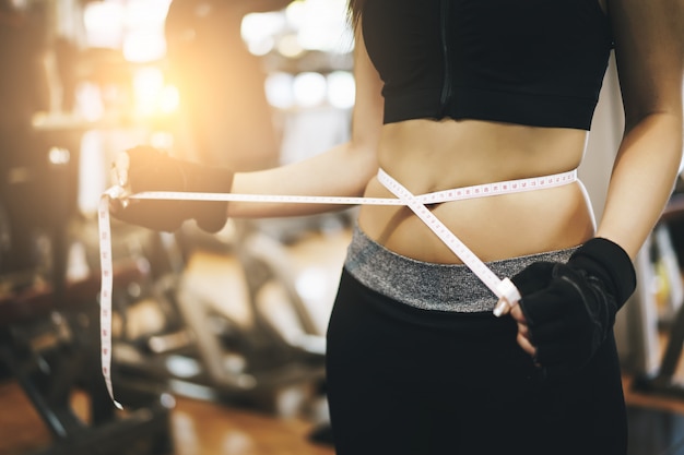 Dünne Frau, die Maßbandverpackung um Taille an einer Turnhalle verwendet. Sport, Fitness, Ernährungsergebnisse, aktiver Lebensstil.