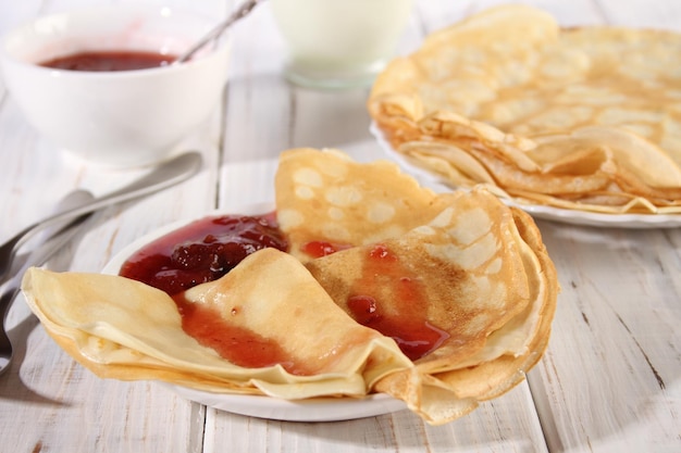 Dünne heiße Pfannkuchen mit Erdbeermarmelade auf einem weißen Holztisch Urlaub Maslenitsa