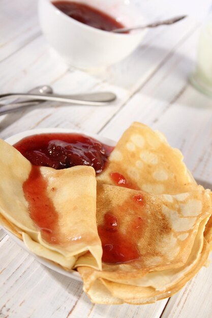 Dünne heiße Pfannkuchen mit Erdbeermarmelade auf einem weißen Holztisch Urlaub Maslenitsa