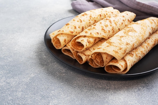 Dünne Pfannkuchen, die auf einem Teller zu einer Rolle gerollt werden Das Konzept eines köstlichen Frühstücks oder Maslenitsa Betonhintergrund