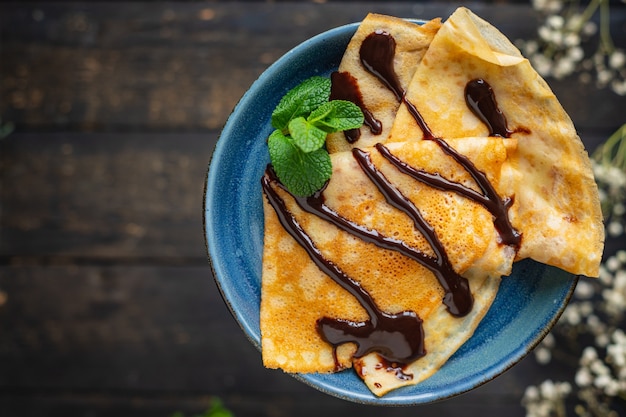 Dünne Pfannkuchen gießen Schokoladenkreppsirup weißen Teller flachen Kuchen