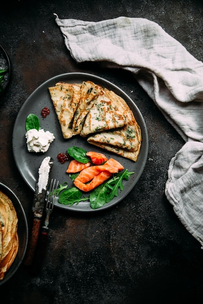 Dünne Pfannkuchen mit Kräutern, Lachs und Frischkäse auf einem Teller