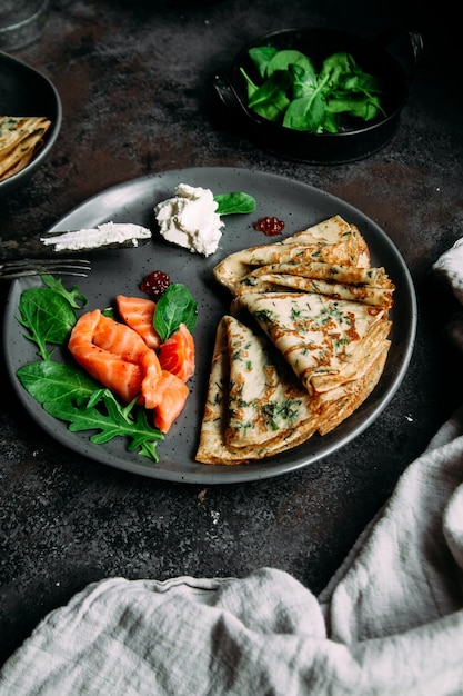 Dünne Pfannkuchen mit Kräutern, Lachs und Frischkäse auf einem Teller