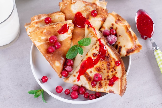 Dünne Pfannkuchen oder Crepes auf einem Teller mit Marmelade und gefrorenen Beeren, Minze. Traditionelles Frühstück oder Dessert.