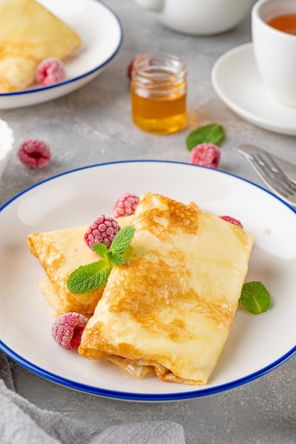 dünne Pfannkuchen oder Crêpes mit Hüttenkäse, Honig, Sauerrahm und Himbeeren Essen für Maslenitsa