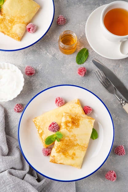 Dünne Pfannkuchen oder Crêpes mit Hüttenkäse-Honig-Sauerrahm und Himbeeren mit einer Tasse Tee