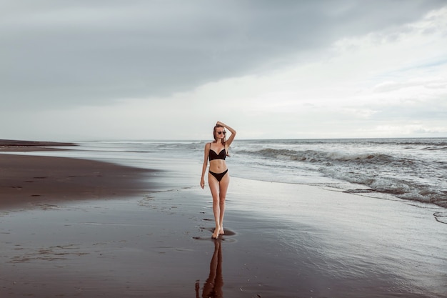 Dünnes Mädchen in einem Badeanzug geht auf den schwarzen Strand