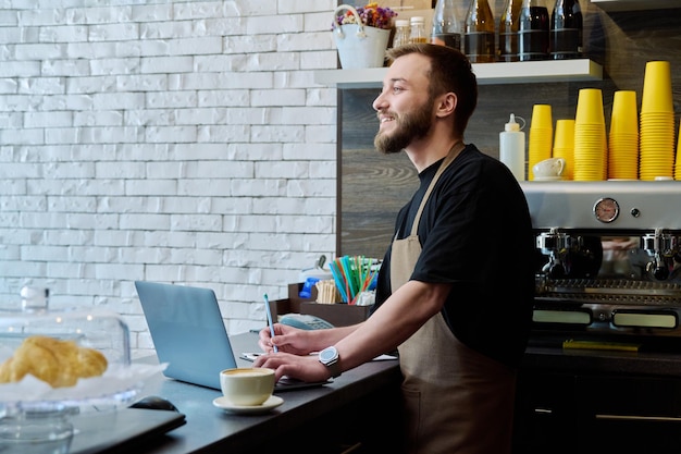 El dueño de la cafetería trabaja con un hombre joven con una computadora portátil en el mostrador.