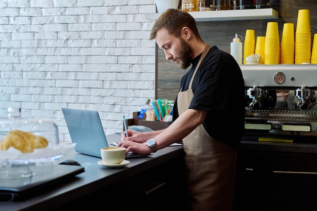 El dueño de la cafetería trabaja con un hombre joven con una computadora portátil en el mostrador.