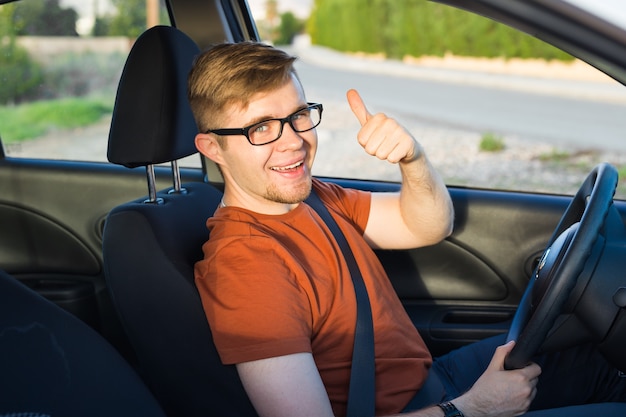 El dueño del coche feliz está mostrando los pulgares hacia arriba dentro de su nuevo coche.