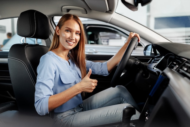 Dueño de coche nuevo mujer feliz sentado en el asiento del conductor