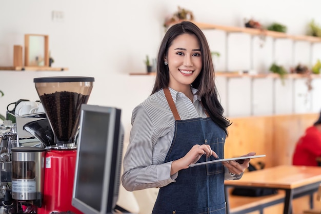 Dueño de la empresaria asiática joven hermosa que sostiene una tableta en un café. Mirando a la cámara.