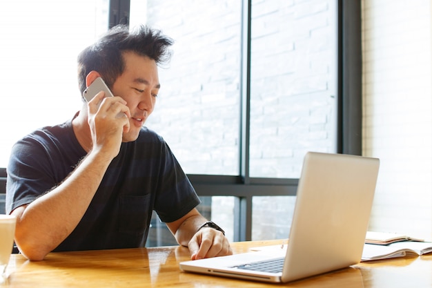 Dueño de negocio pequeño masculino asiático alegre que habla en el teléfono con el cliente