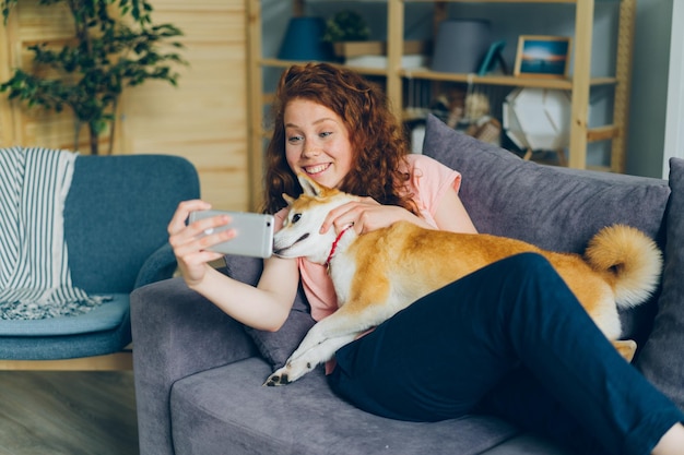 Dueño de perro joven tomando selfie con mascota sonriendo usando cámara de teléfono inteligente en casa