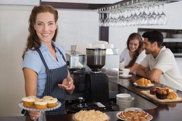 Dueño sonriente del café que sostiene bocados dulces con los pares en el contador en cafetería