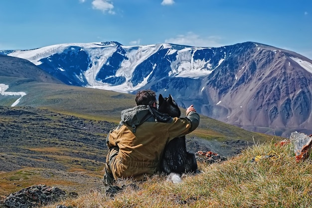 El dueño con su amado perro husky se sienta en una colina y señala con la mano las montañas