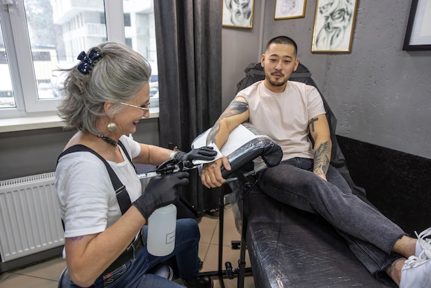 Dueño de un tatuaje canoso trabajando con el cliente