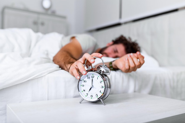 Duerme más. Concepto de salud. Etapas del sueño. Hombre despierto infeliz con la alarma sonando. Aunque duerma, es posible que se despierte sintiéndose como si no hubiera dormido en absoluto.