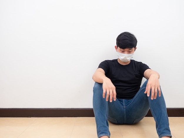 Düsterer asiatischer Mann mit Maske sitzt auf dem Boden und berührt seinen Kopf auf weißem Hintergrund