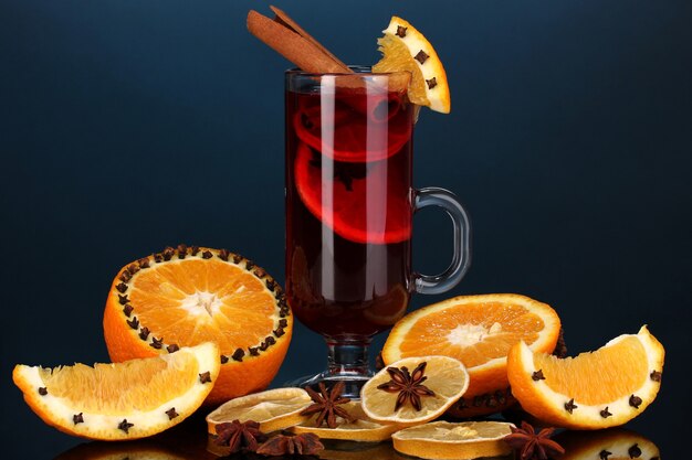 Duftender Glühwein im Glas mit Gewürzen und Orangen auf blauem Hintergrund