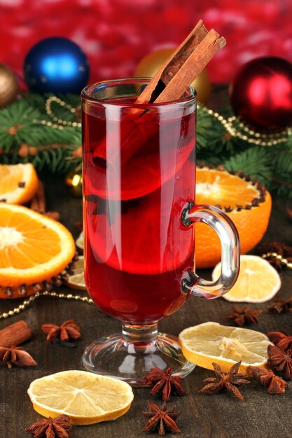 Duftender Glühwein im Glas mit Gewürzen und Orangen auf Holztisch auf roter Oberfläche