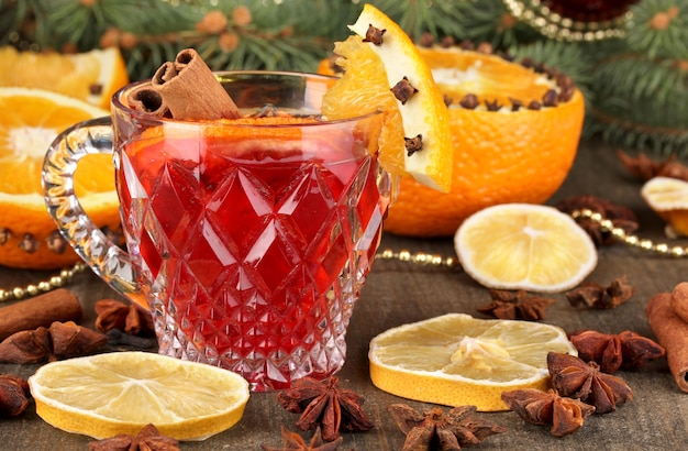 Duftender Glühwein im Glas mit Gewürzen und Orangen auf Holztisch