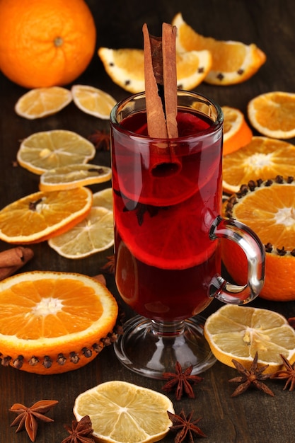 Duftender Glühwein im Glas mit Gewürzen und Orangen auf Holztisch