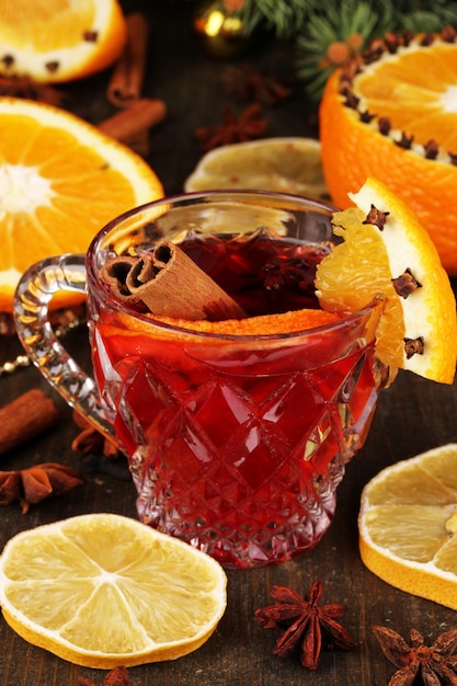 Duftender Glühwein im Glas mit Gewürzen und Orangen auf Holztisch