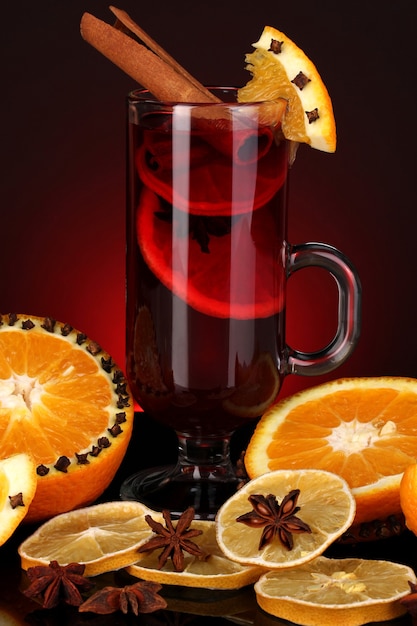 Duftender Glühwein im Glas mit Gewürzen und Orangen auf rotem Grund