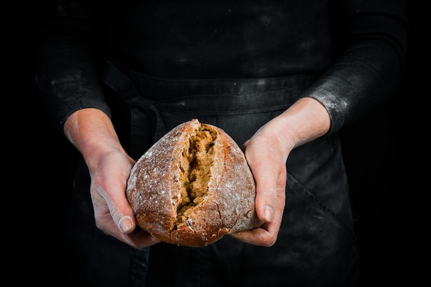 Duftendes Ciabatta in Frauenhänden, Rezeptidee für Lebensmittelfotografie. Schwarzer backender Hintergrund.