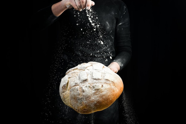 Duftendes Weißbrot in den Händen der Frauen. Backhintergrund aus schwarzem Mehl.