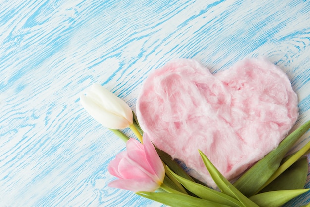 Dulce algodón de azúcar y delicados tulipanes rosas en forma de corazón sobre fondo de madera azul. Copia espacio