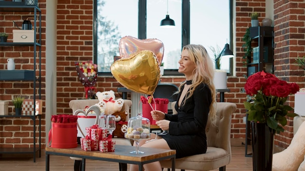 Dulce atractiva mujer elegante sosteniendo un globo en forma de corazón disfrutando de un hermoso regalo de un novio romántico celebrando el día de San Valentín anunciando un regalo floral. Concepto de decoración de aniversario.