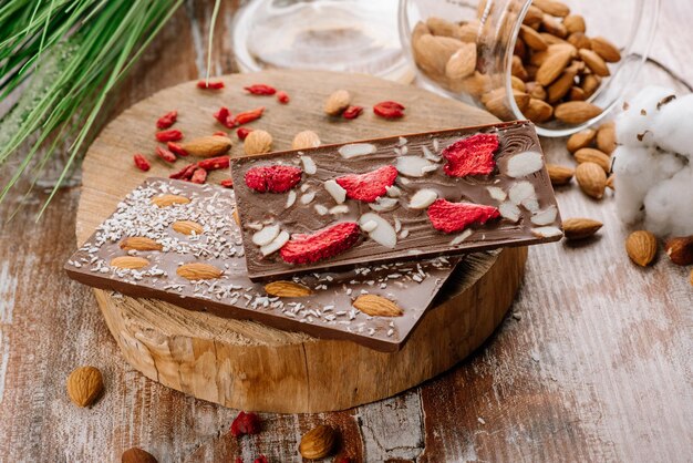 Dulce barra de chocolate con frutas y nueces en el fondo de madera