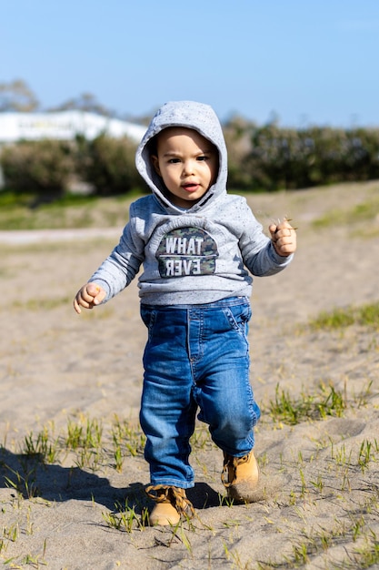 Dulce bebé con capucha y jeans caminando y jugando en la arena Actividad con un niño pequeño