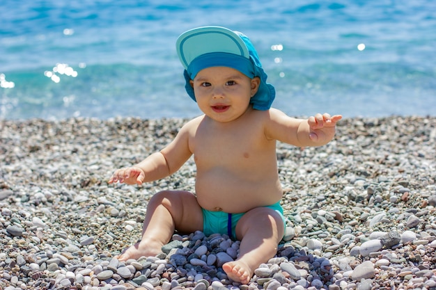 Dulce bebé gordito en una playa de guijarros. Mar azul y sol de verano