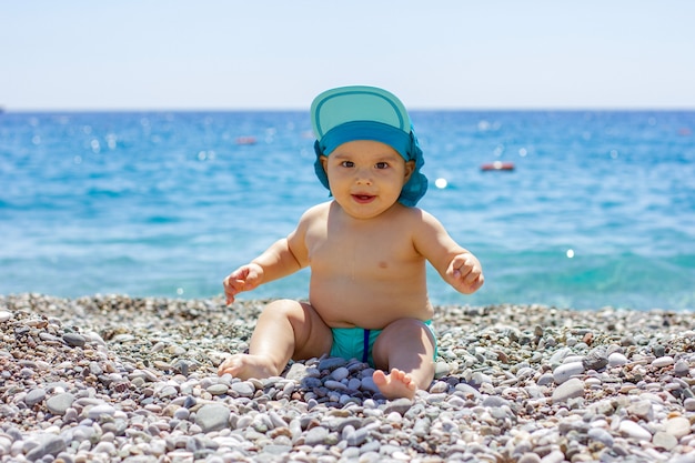 Dulce bebé gordito en una playa de guijarros. Mar azul y sol de verano
